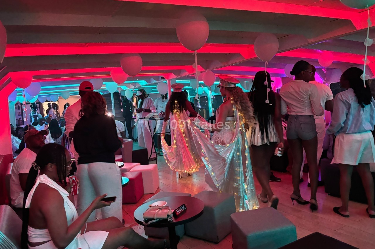 Personnes en tenue blanche et festive dans une salle éclairée de lumières rouges et bleues, décorée de ballons.