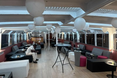 Salle intérieure d'un bateau aménagée avec des tables, des fauteuils et des ballons suspendus au plafond.