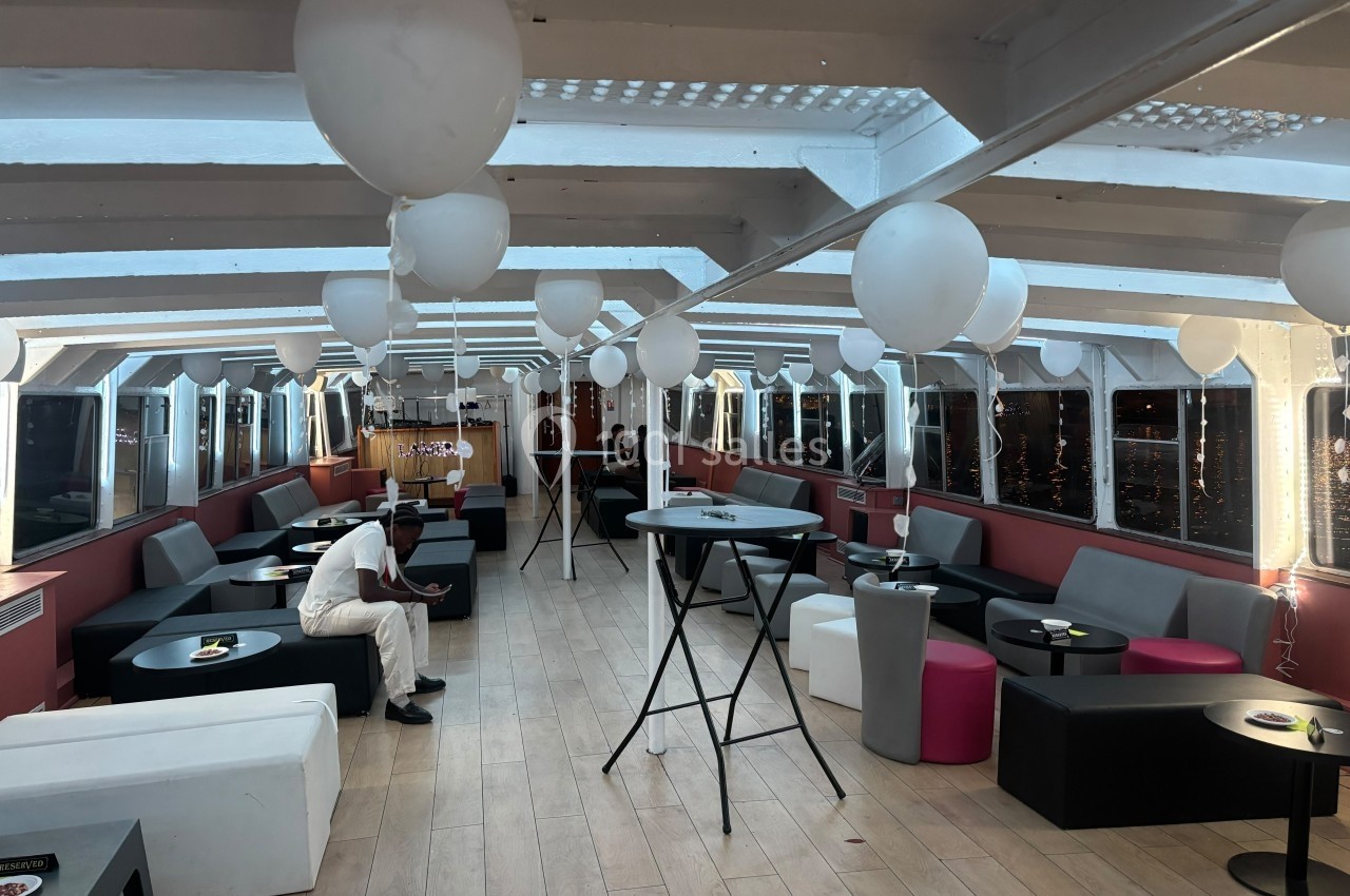 Salle lumineuse décorée de ballons blancs, avec des tables hautes et des banquettes modernes, prête pour un événement.