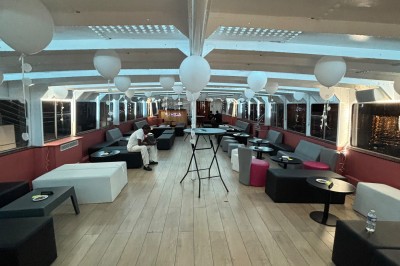 Salle intérieure d'un bateau aménagée avec des tables, des fauteuils et des ballons suspendus au plafond.