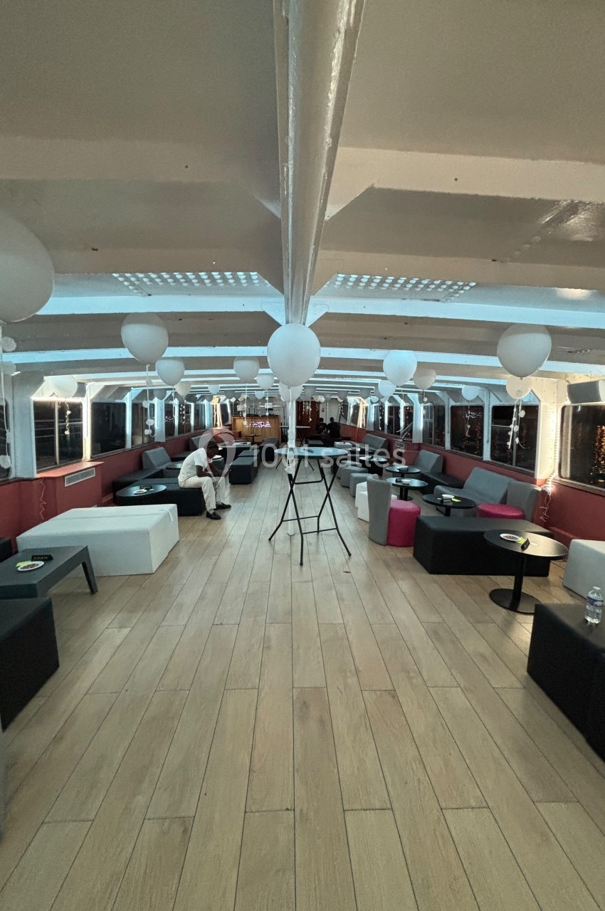 Intérieur d'un bateau aménagé avec des canapés, tables basses et ballons suspendus, éclairé par des lumières tamisées.