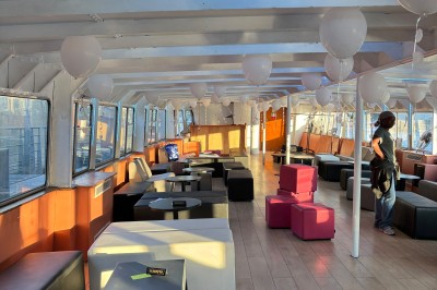 Salle intérieure d'un bateau aménagée avec des tables, des fauteuils et des ballons suspendus au plafond.