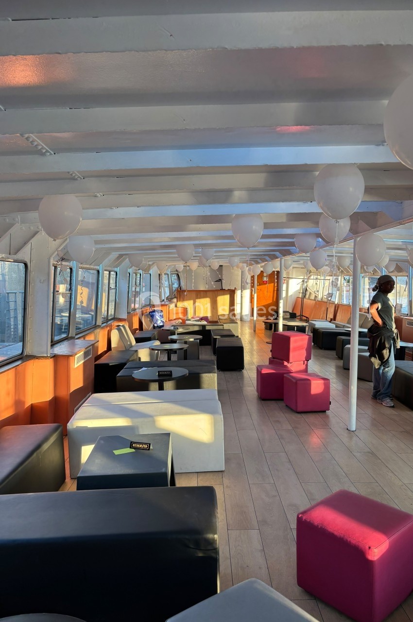 Intérieur lumineux d'un bateau aménagé avec des banquettes colorées, des tables basses et des ballons suspendus.