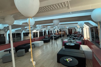 Salle intérieure d'un bateau aménagée avec des tables, des fauteuils et des ballons suspendus au plafond.