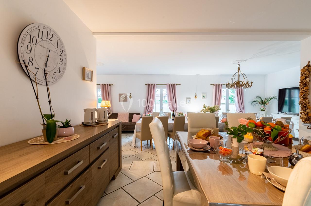 Salle à manger lumineuse avec table dressée, chaises blanches, buffet en bois et décoration chaleureuse.