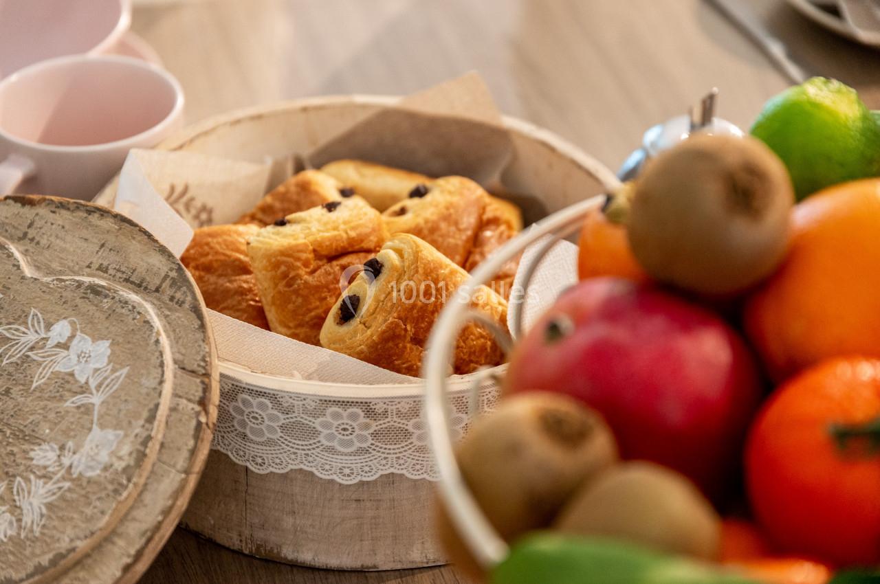 Assortiment de viennoiseries dans un panier en bois, entouré de fruits frais sur une table.