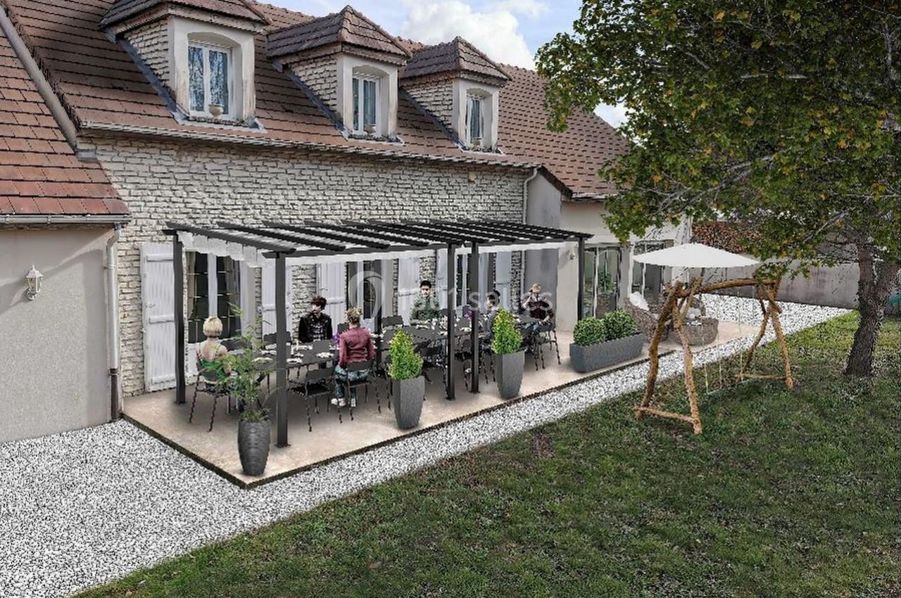 Terrasse aménagée avec pergola, mobilier de jardin et plantes en pot, attenante à une maison en pierre.