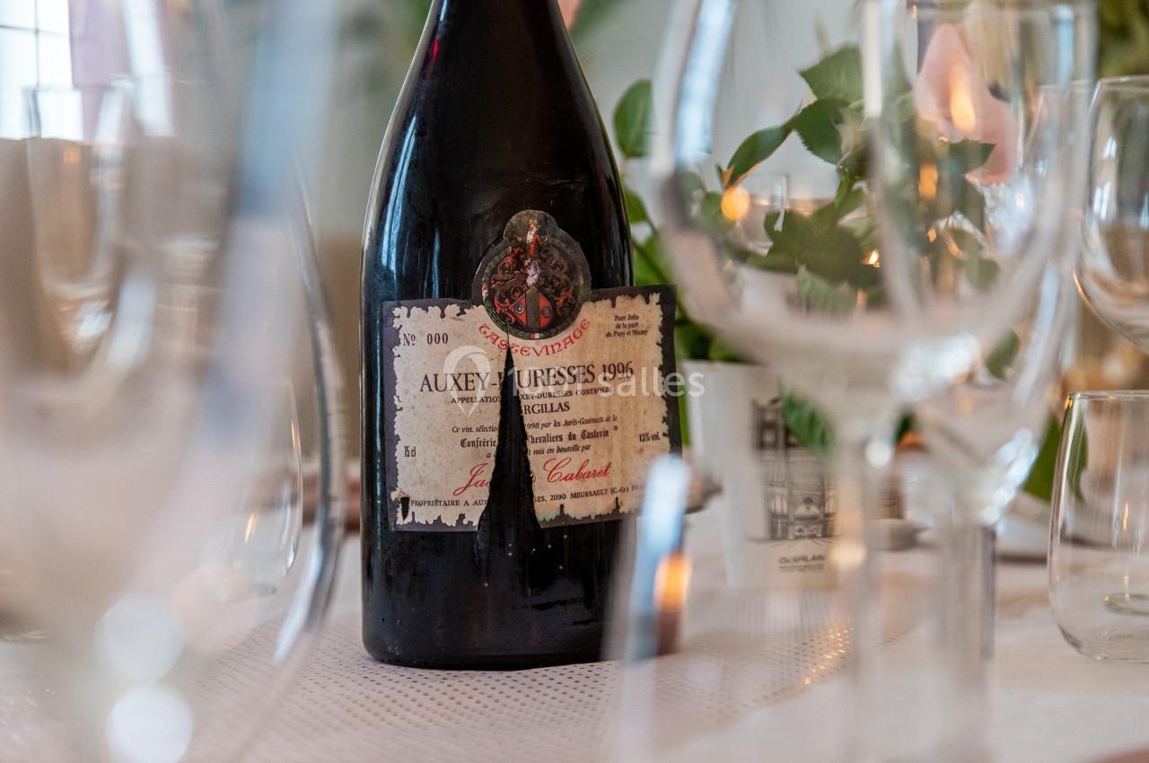 Bouteille de vin Auxey-Duresses 1996 posée sur une table dressée avec des verres et des décorations végétales.