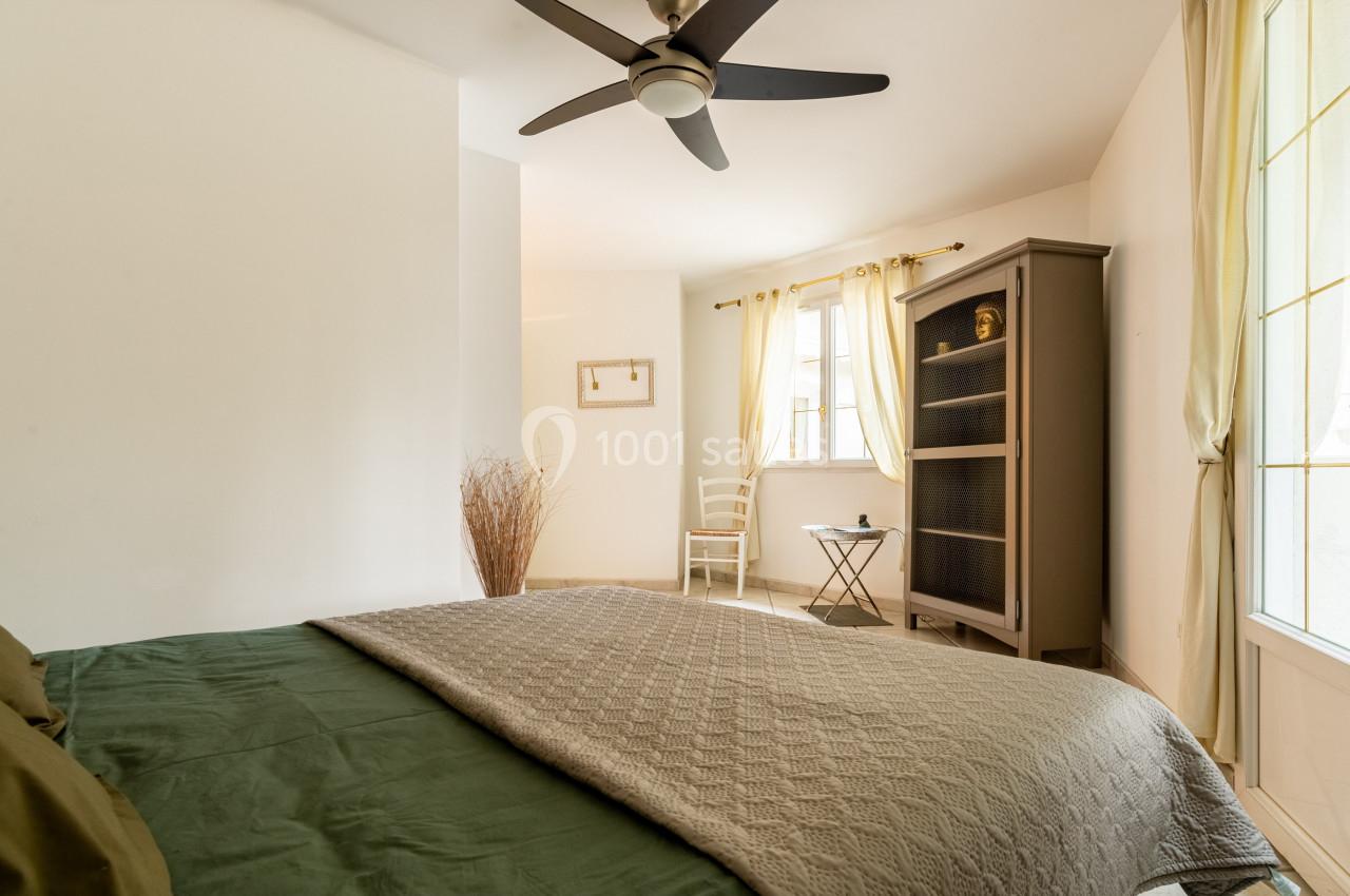 Chambre lumineuse avec lit double, armoire, chaise et table près d'une fenêtre aux rideaux clairs.