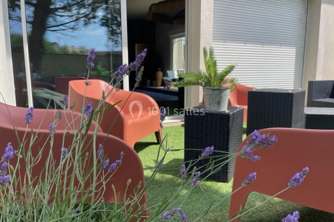 Mobilier de jardin avec fauteuils rouges et table noire sur une terrasse en gazon artificiel, lavandes au premier plan.