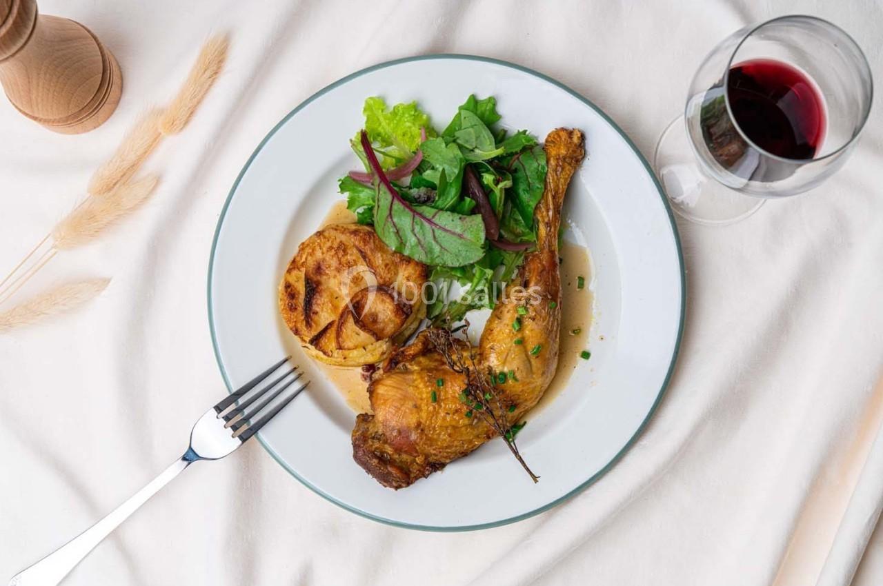 Assiette contenant une cuisse de volaille rôtie, gratin de pommes de terre, salade verte et un verre de vin rouge à côté.