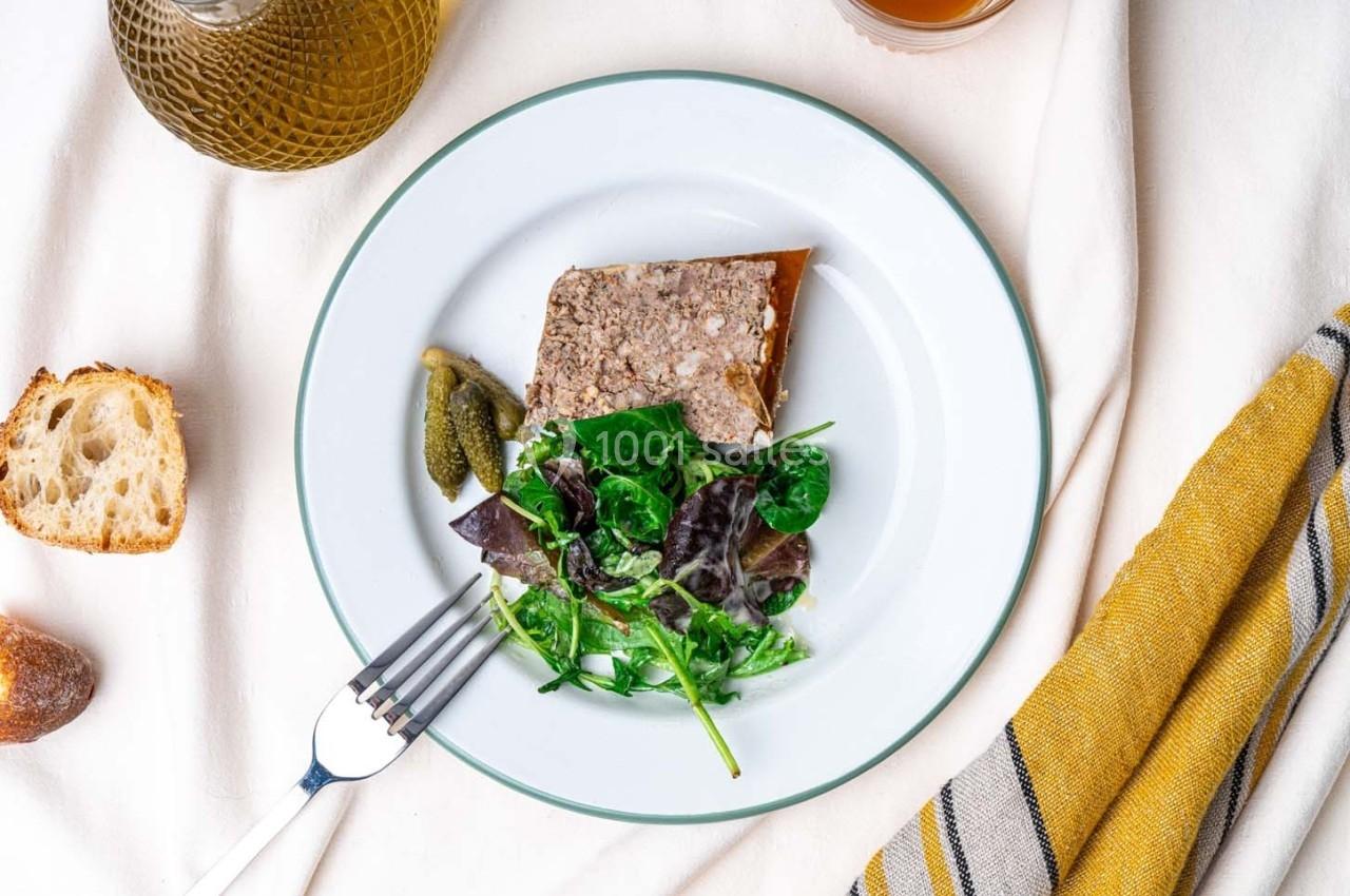Assiette contenant une tranche de pâté, des cornichons et une salade verte, avec une fourchette et une serviette à rayures.