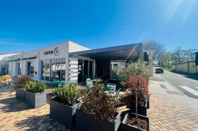 Terrasse extérieure d'un café avec tables et chaises vertes, entourée de plantes, sous un ciel ensoleillé.