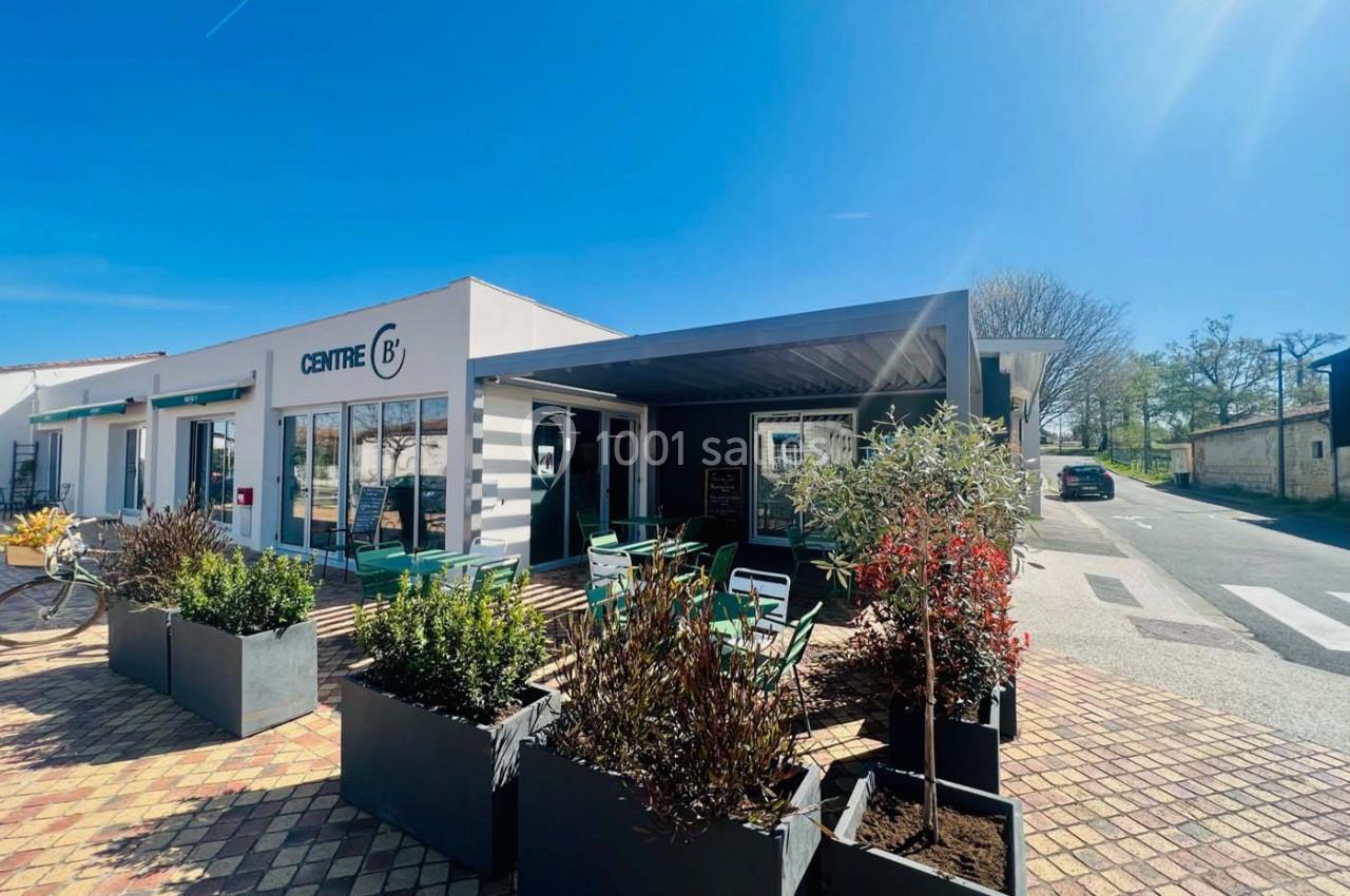 Façade d'un bâtiment moderne avec terrasse aménagée, plantes en pots et ciel dégagé en arrière-plan.
