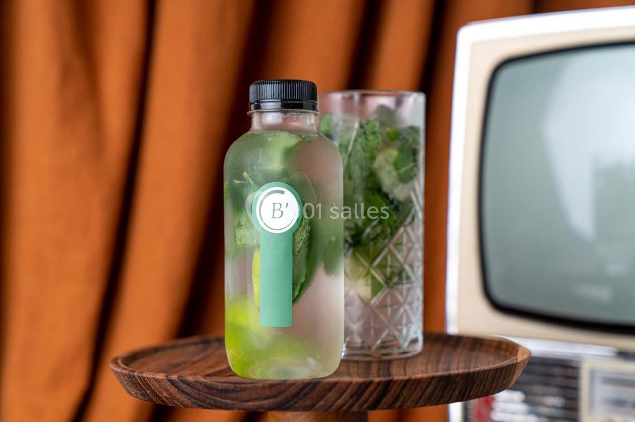 Bouteille en verre remplie d'eau infusée aux herbes et citron, posée sur un plateau en bois devant un verre et une…