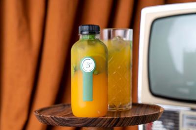 Terrasse extérieure d'un café avec tables et chaises vertes, entourée de plantes, sous un ciel ensoleillé.