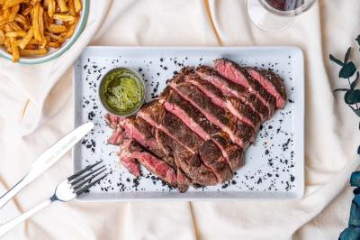 Terrasse extérieure d'un café avec tables et chaises vertes, entourée de plantes, sous un ciel ensoleillé.