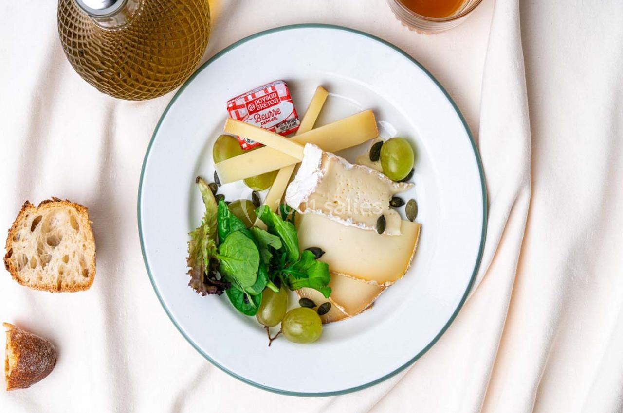 Assiette de fromages variés avec raisins, salade verte et graines, accompagnée de pain et d'huile d'olive.