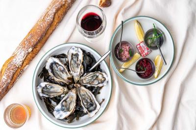 Terrasse extérieure d'un café avec tables et chaises vertes, entourée de plantes, sous un ciel ensoleillé.
