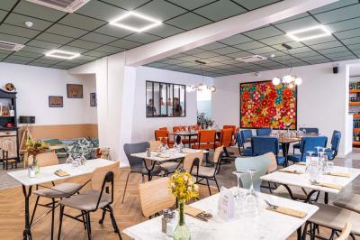 Terrasse extérieure d'un café avec tables et chaises vertes, entourée de plantes, sous un ciel ensoleillé.
