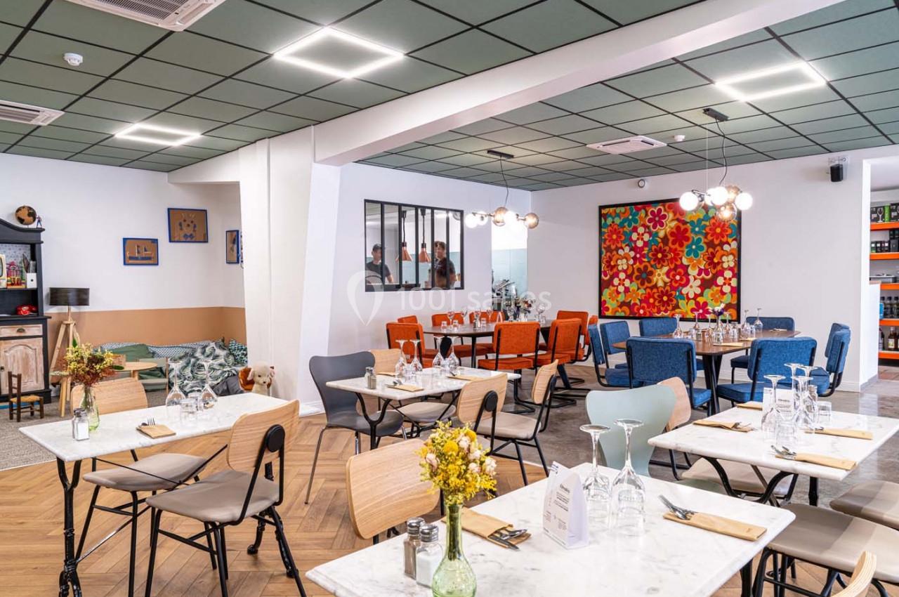 Salle de restaurant lumineuse avec tables dressées, chaises variées et décoration colorée sur les murs.