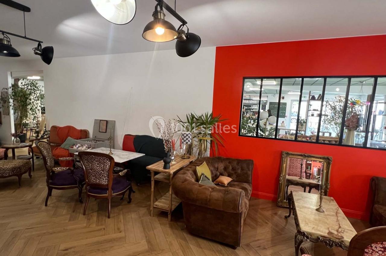 Espace intérieur chaleureux avec mobilier éclectique, murs blancs et rouges, et grande verrière donnant sur une autre pièce.