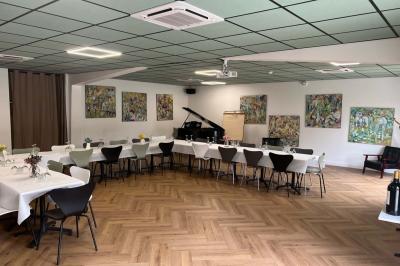 Terrasse extérieure d'un café avec tables et chaises vertes, entourée de plantes, sous un ciel ensoleillé.
