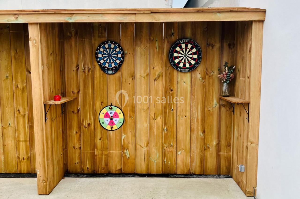 Trois cibles de fléchettes fixées sur une cloison en bois, avec une étagère contenant un vase et une pomme.