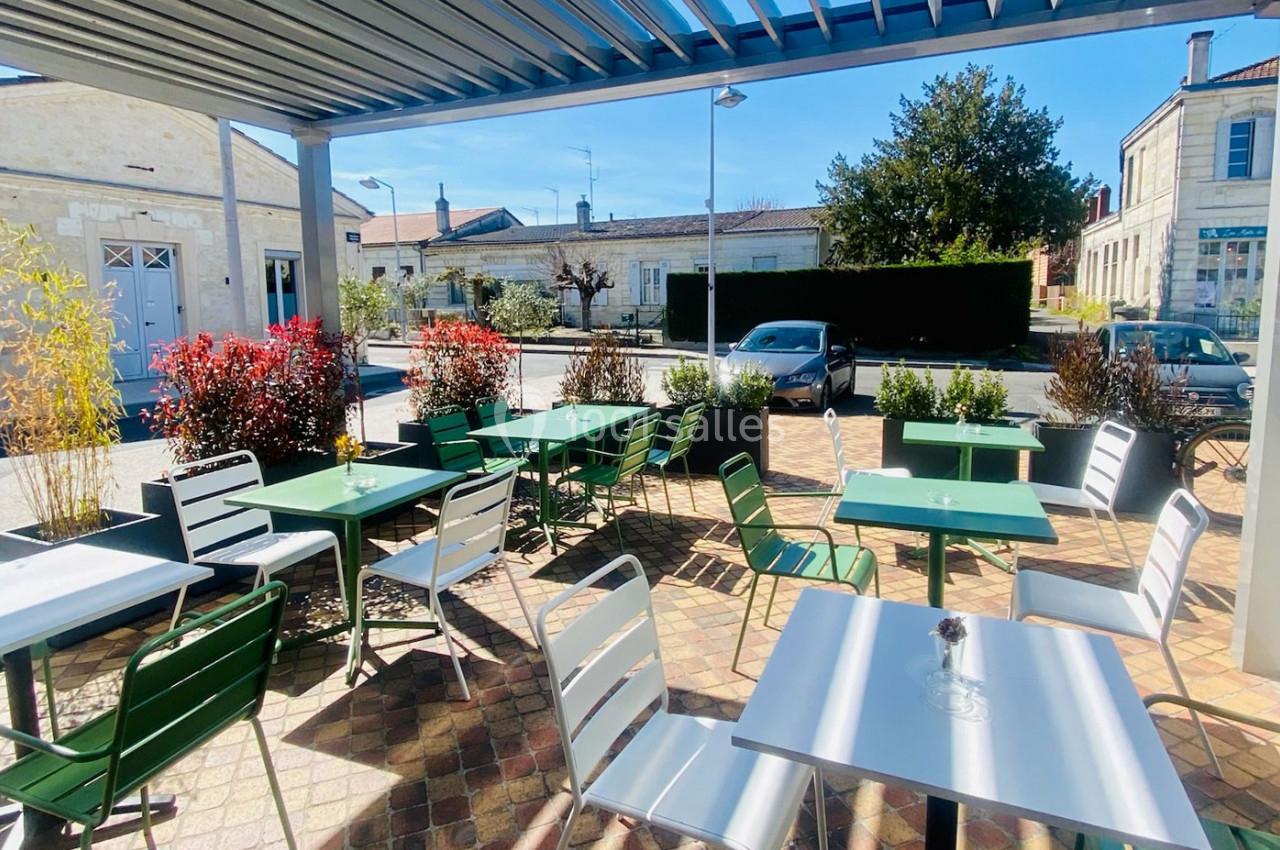 Terrasse extérieure avec tables et chaises vertes et blanches, entourée de plantes, sous un ciel bleu clair.