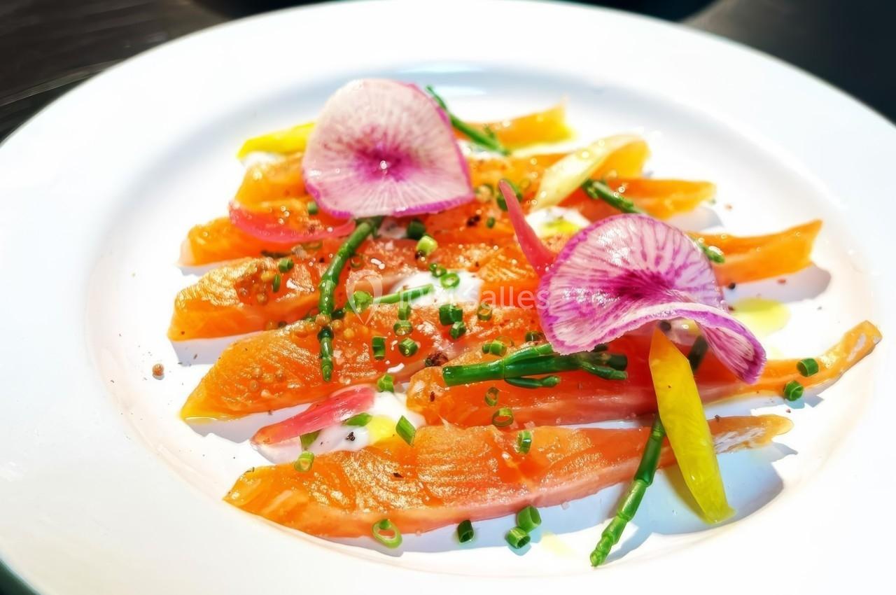 Tranches de saumon fumé garnies de radis roses, ciboulette, salicornes et filet d'huile sur une assiette blanche.