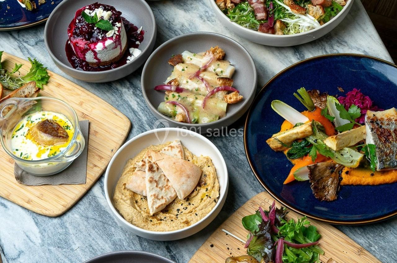 Assortiment de plats variés comprenant légumes, houmous, poisson grillé et desserts, disposés sur une table en marbre.