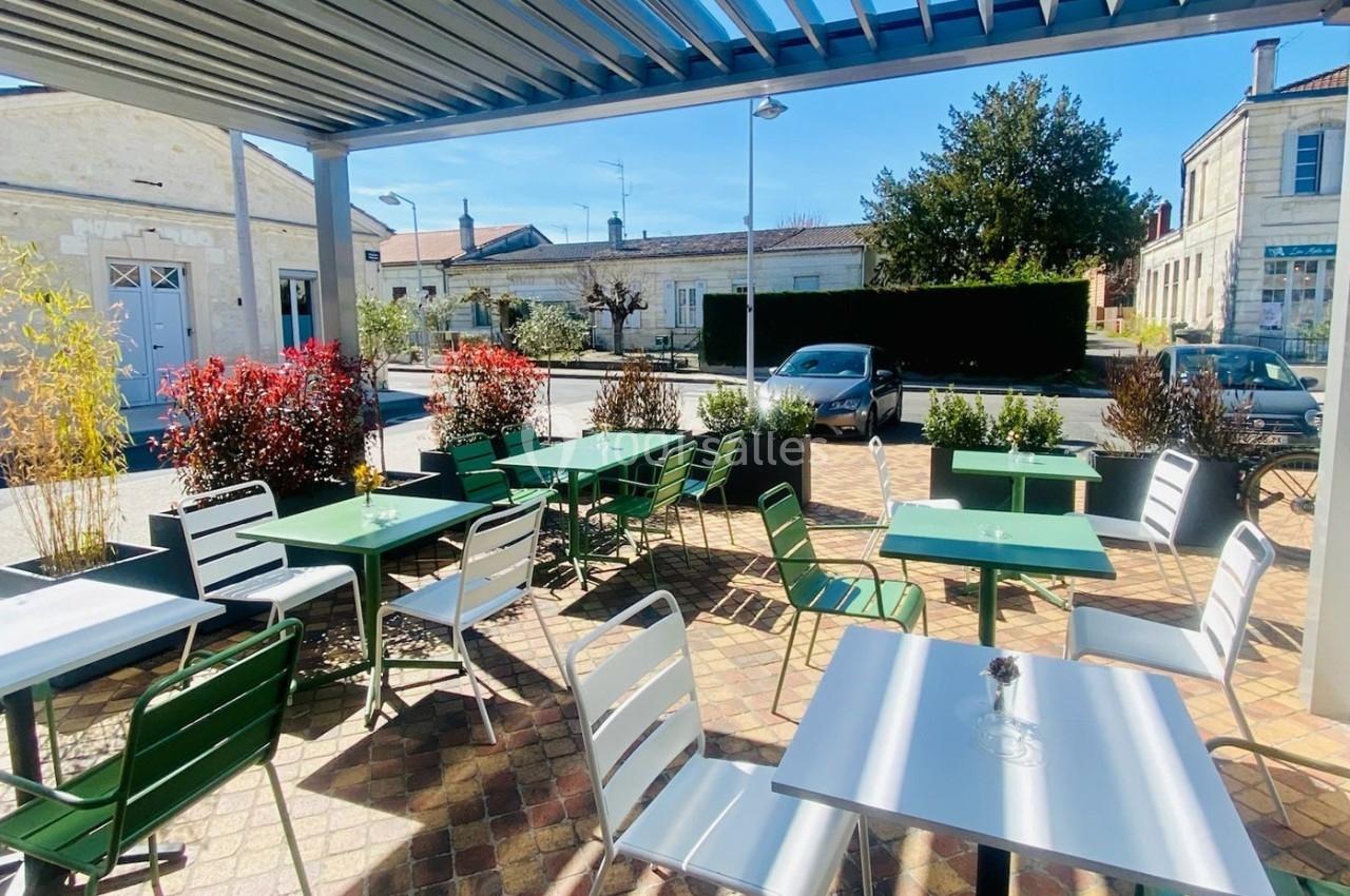 Terrasse extérieure avec tables et chaises vertes et blanches, entourée de plantes et baignée de lumière naturelle.