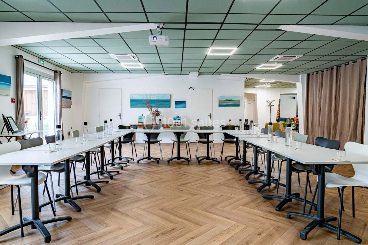Salle de réunion lumineuse avec tables disposées en U, chaises modernes, parquet en bois et décorations murales.