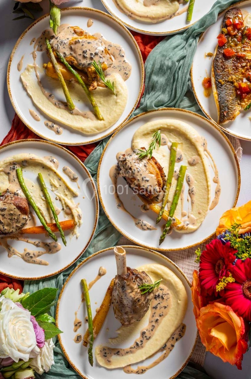 Assiettes garnies de purée, asperges, viande ou poisson, nappées de sauce, disposées sur une table décorée de fleurs.