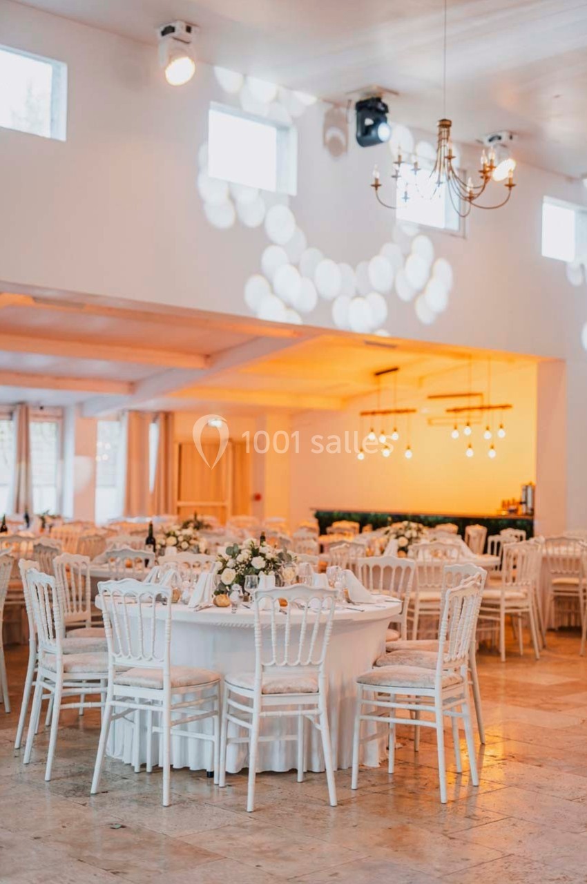 Salle de réception lumineuse avec tables rondes décorées de fleurs blanches et chaises blanches élégantes.