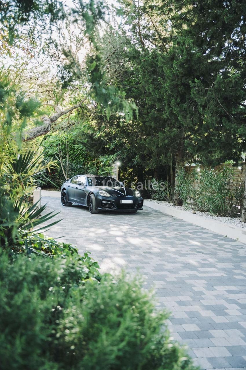 Voiture noire garée sur une allée pavée entourée de végétation et d'arbres.