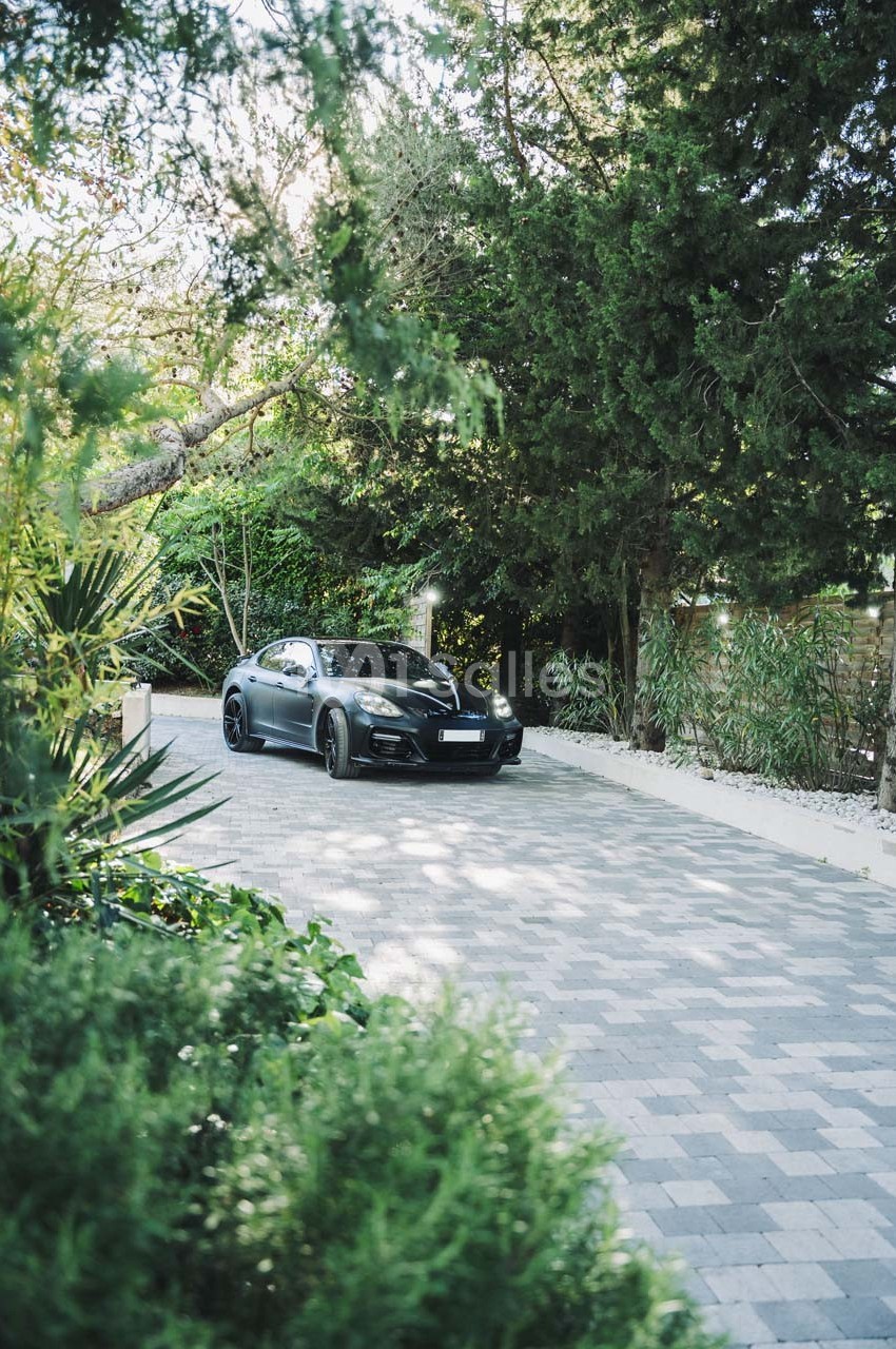 Voiture noire garée sur une allée pavée entourée de végétation et d'arbres.