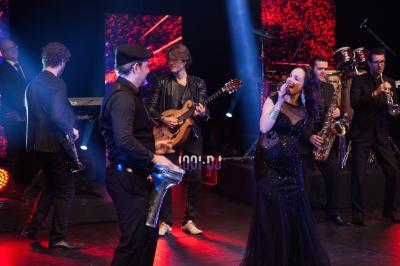 Groupe de musiciens jouant sur scène dans une salle élégante avec un grand lustre et un public dansant.