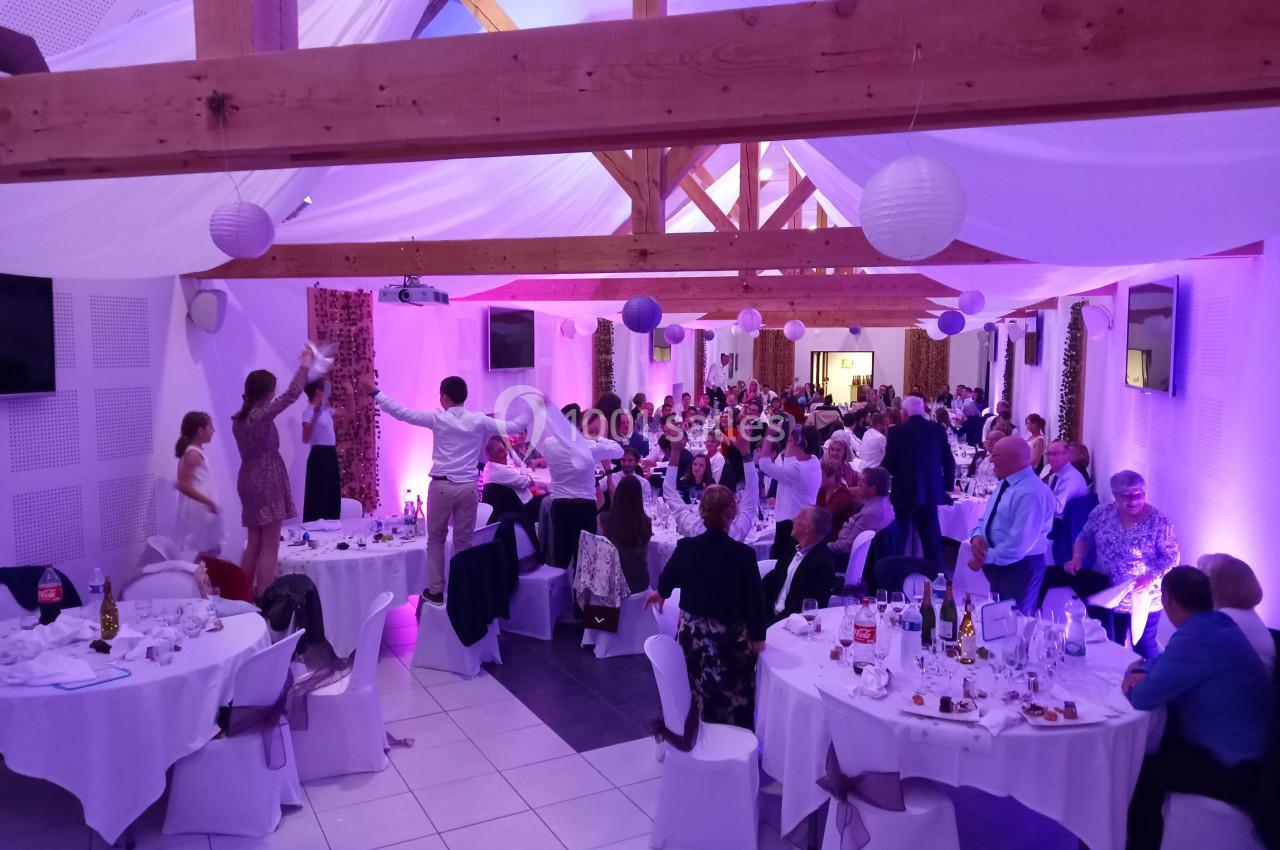 Salle de réception décorée avec des invités assis et debout, ambiance festive sous des lumières violettes.