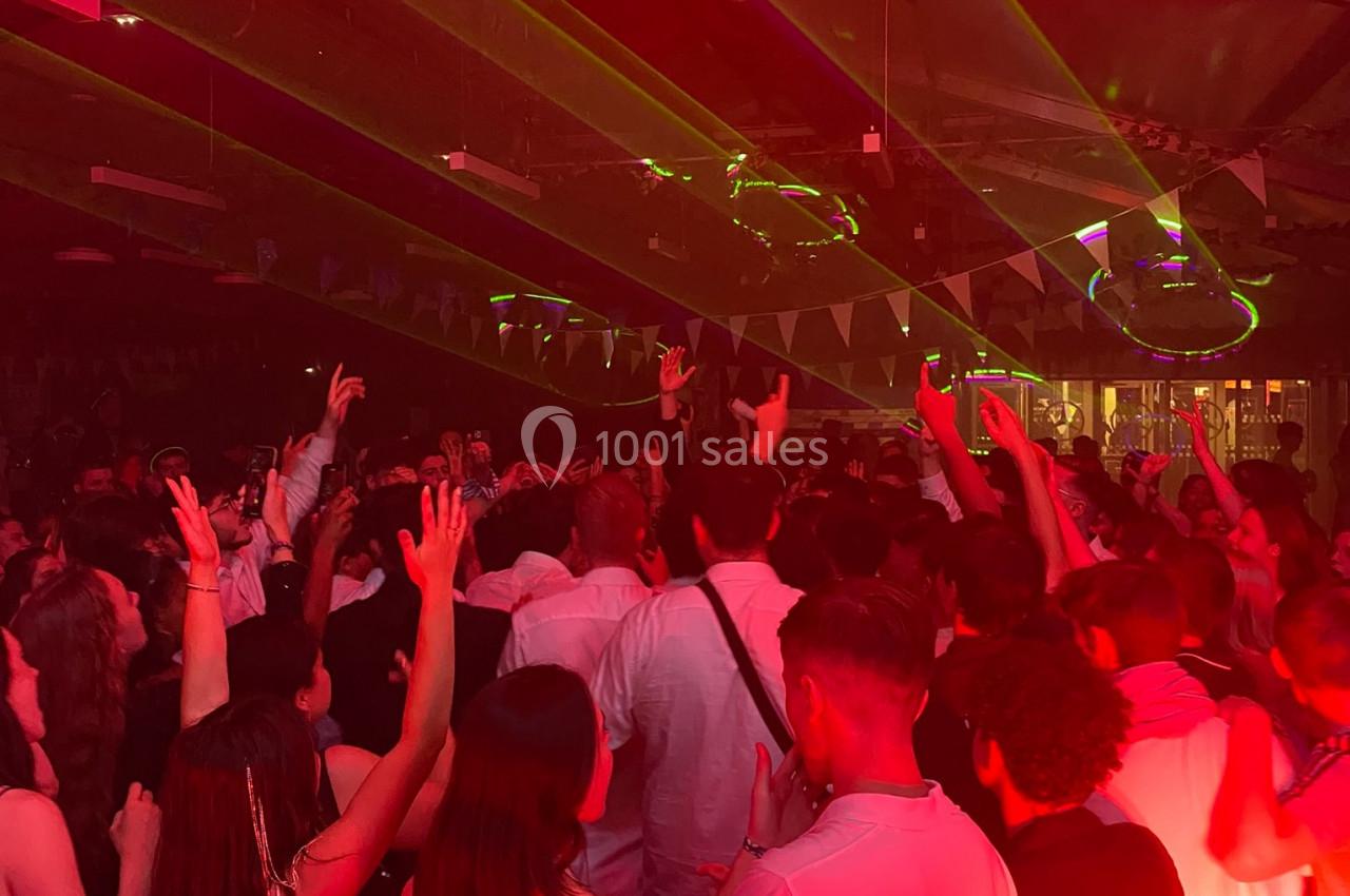 Foule dansante sous des lumières rouges et des faisceaux laser dans une ambiance festive en intérieur.