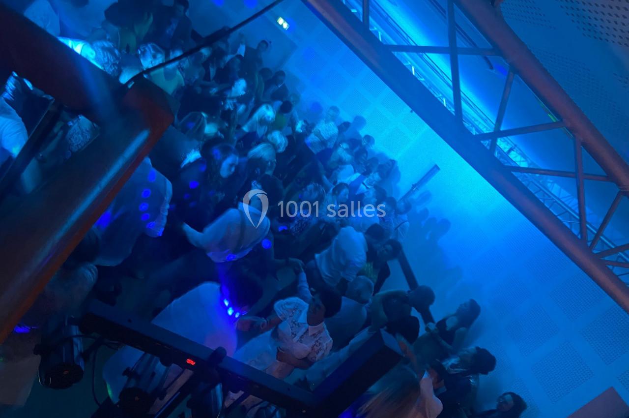 Groupe de personnes dansant dans une salle éclairée par des lumières bleues, ambiance festive et animée.