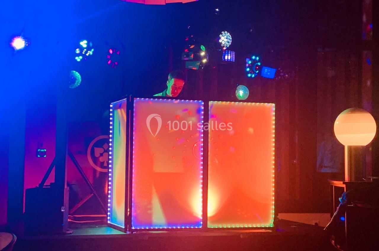 Un DJ mixe derrière une console lumineuse entourée de jeux de lumière colorés dans une ambiance festive.