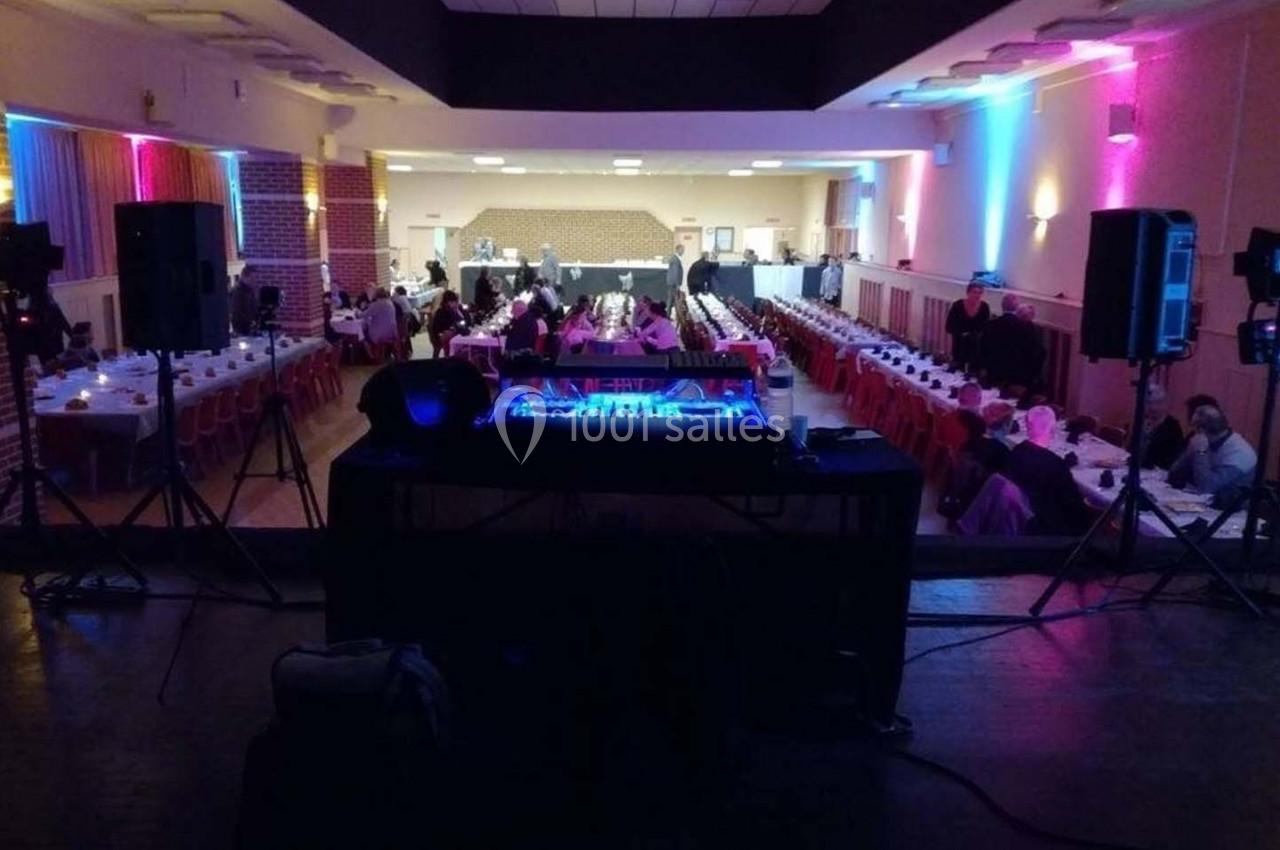 Salle de réception avec tables dressées, vue depuis une scène équipée d'une console de mixage lumineuse.