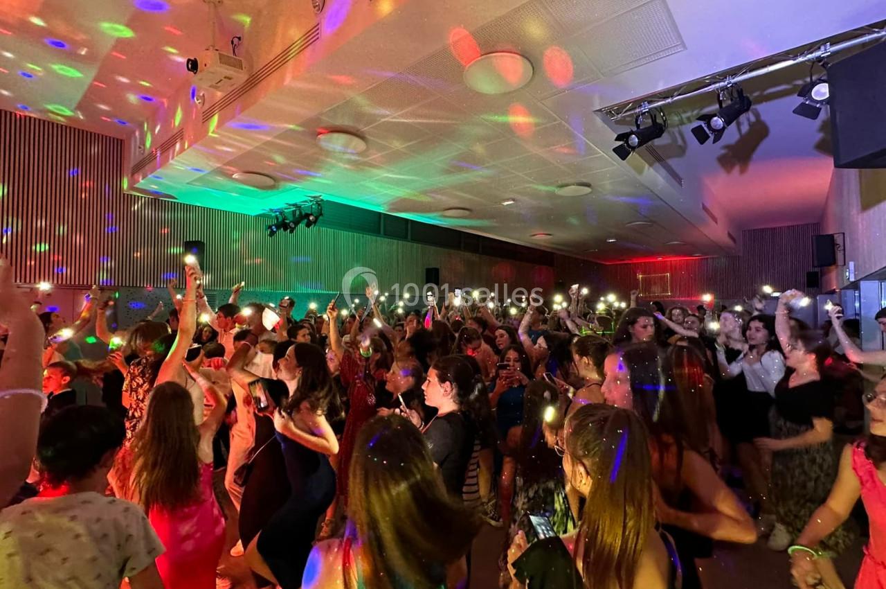 Des personnes dansent dans une salle éclairée par des lumières colorées, certaines brandissant des téléphones allumés.