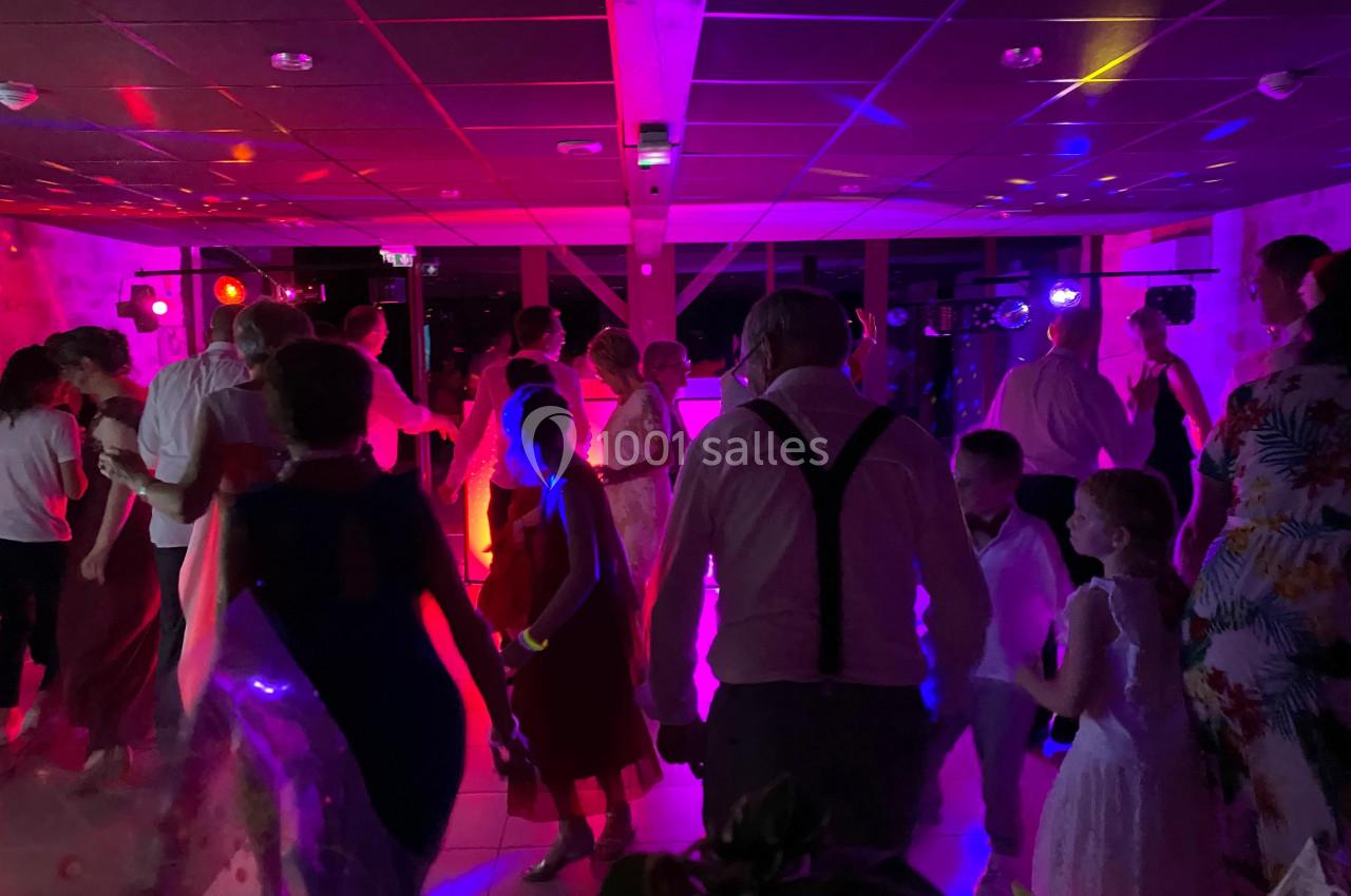 Des personnes dansent dans une salle éclairée par des lumières colorées lors d'une fête ou d'un événement.
