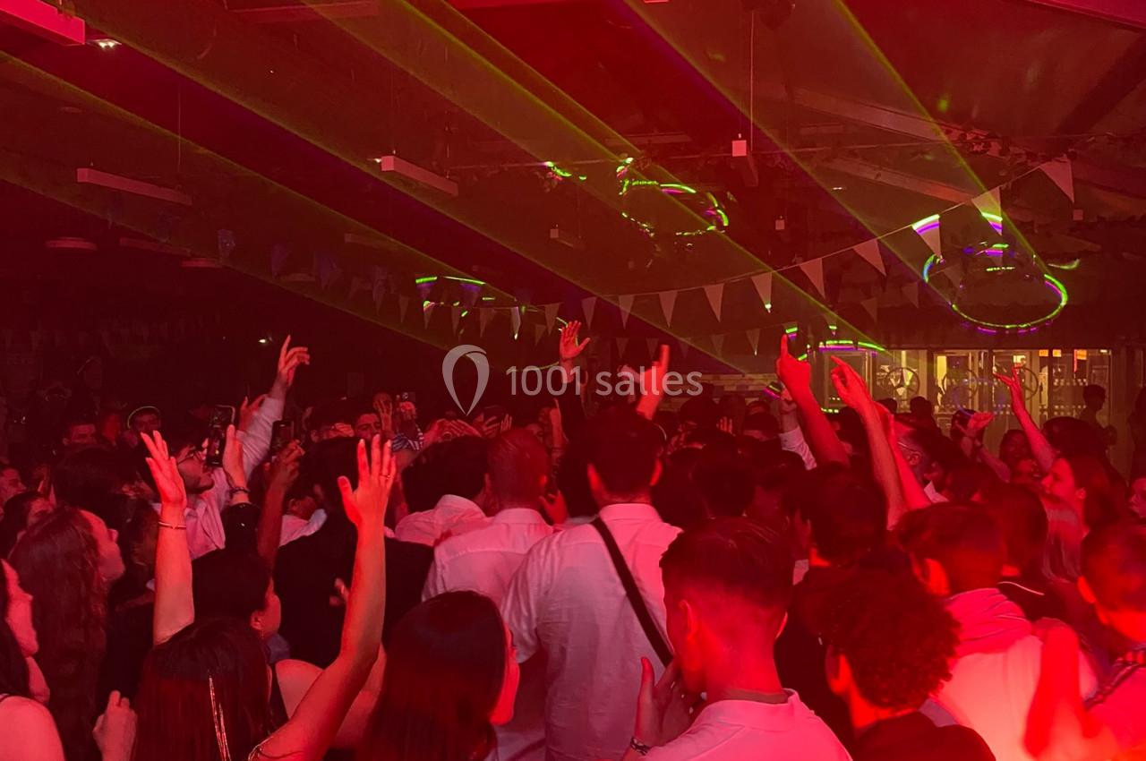 Foule dansante sous des lumières rouges et des lasers dans une ambiance festive en intérieur.