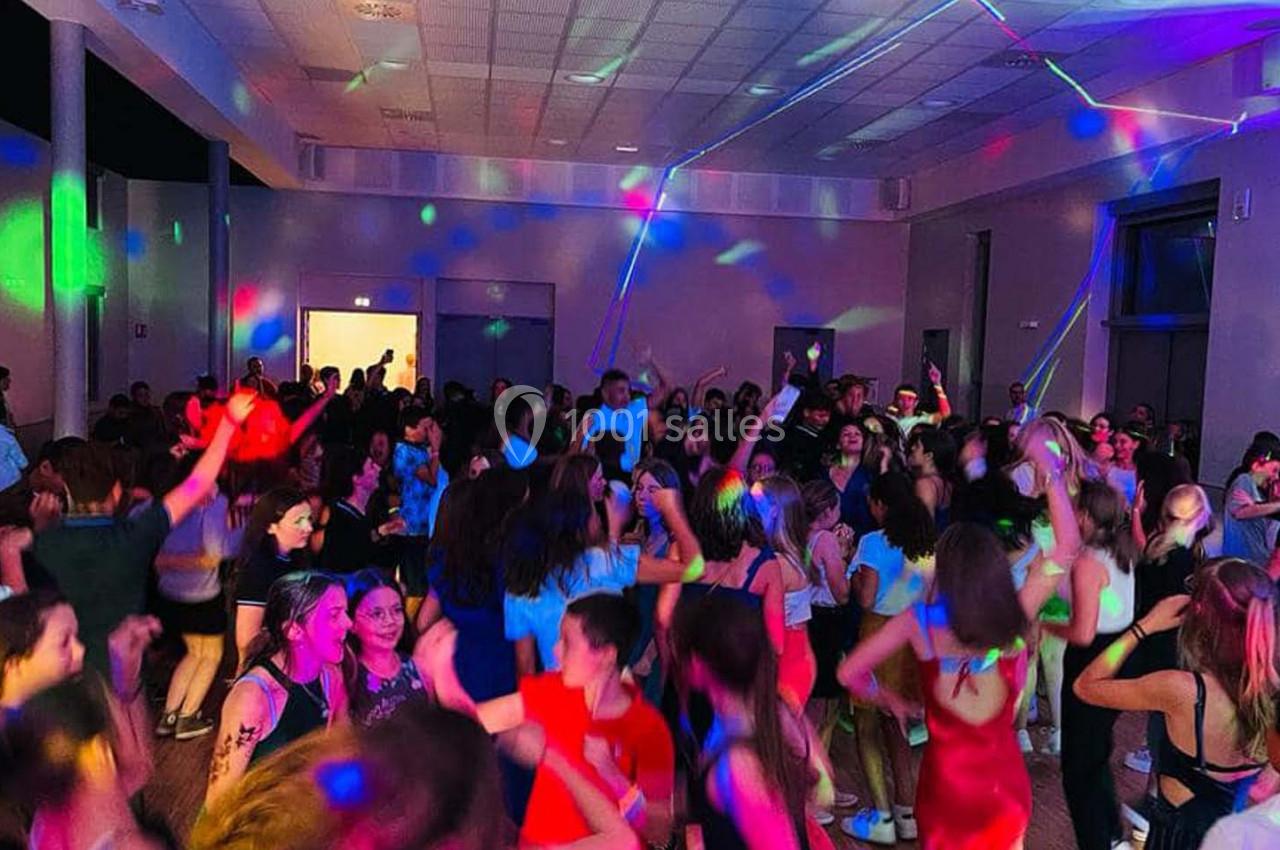 Groupe de personnes dansant dans une salle éclairée par des lumières colorées lors d'une soirée festive.