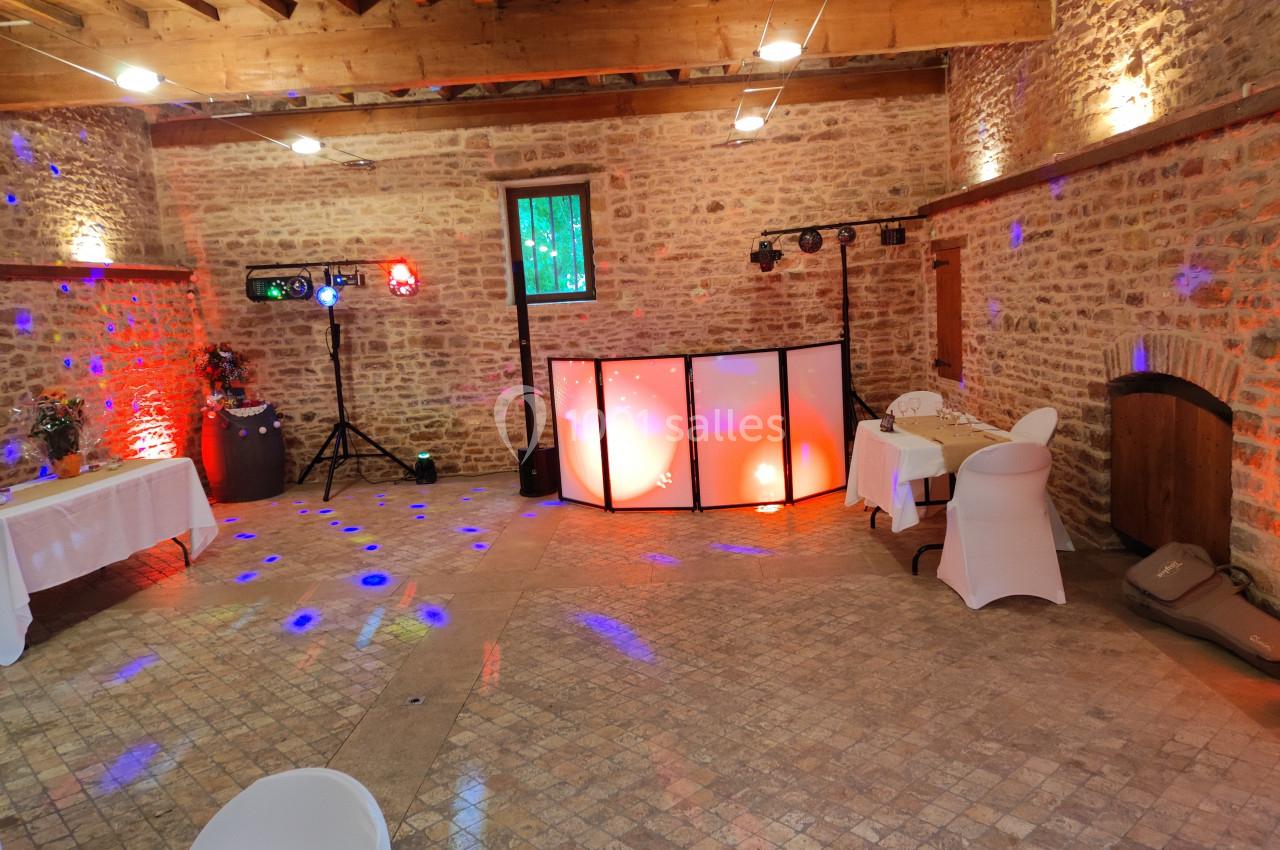 Salle en pierre avec éclairage coloré, tables décorées et espace aménagé pour une animation musicale.