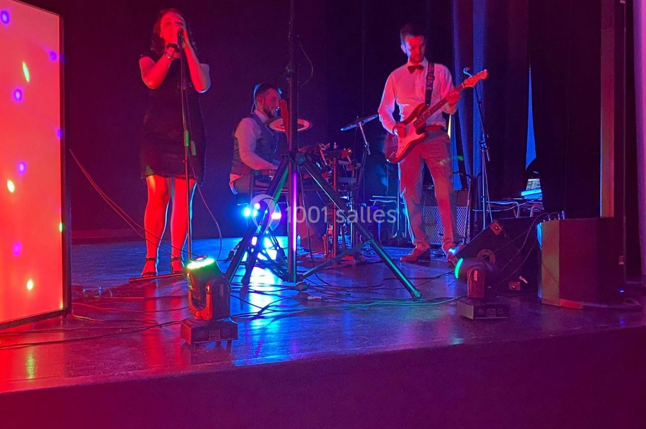 Un groupe de musiciens joue sur une scène éclairée par des lumières colorées dans une ambiance sombre.