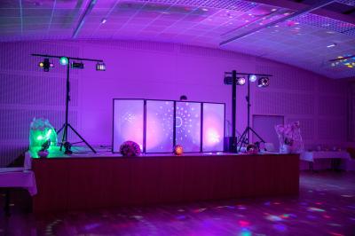 Salle de réception avec tables dressées, vue depuis une scène équipée d'une console de mixage lumineuse.